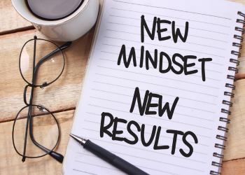 A cup of coffee and glasses next to a notebook which has the words new mindset new results written on it. Mindset is crucial for training high prey drive dogs.